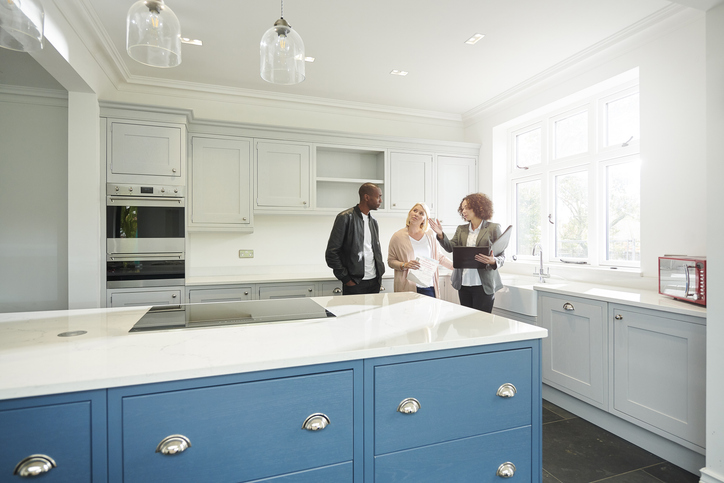 Real estate agent showing a couple a white kitchen with blue drawers